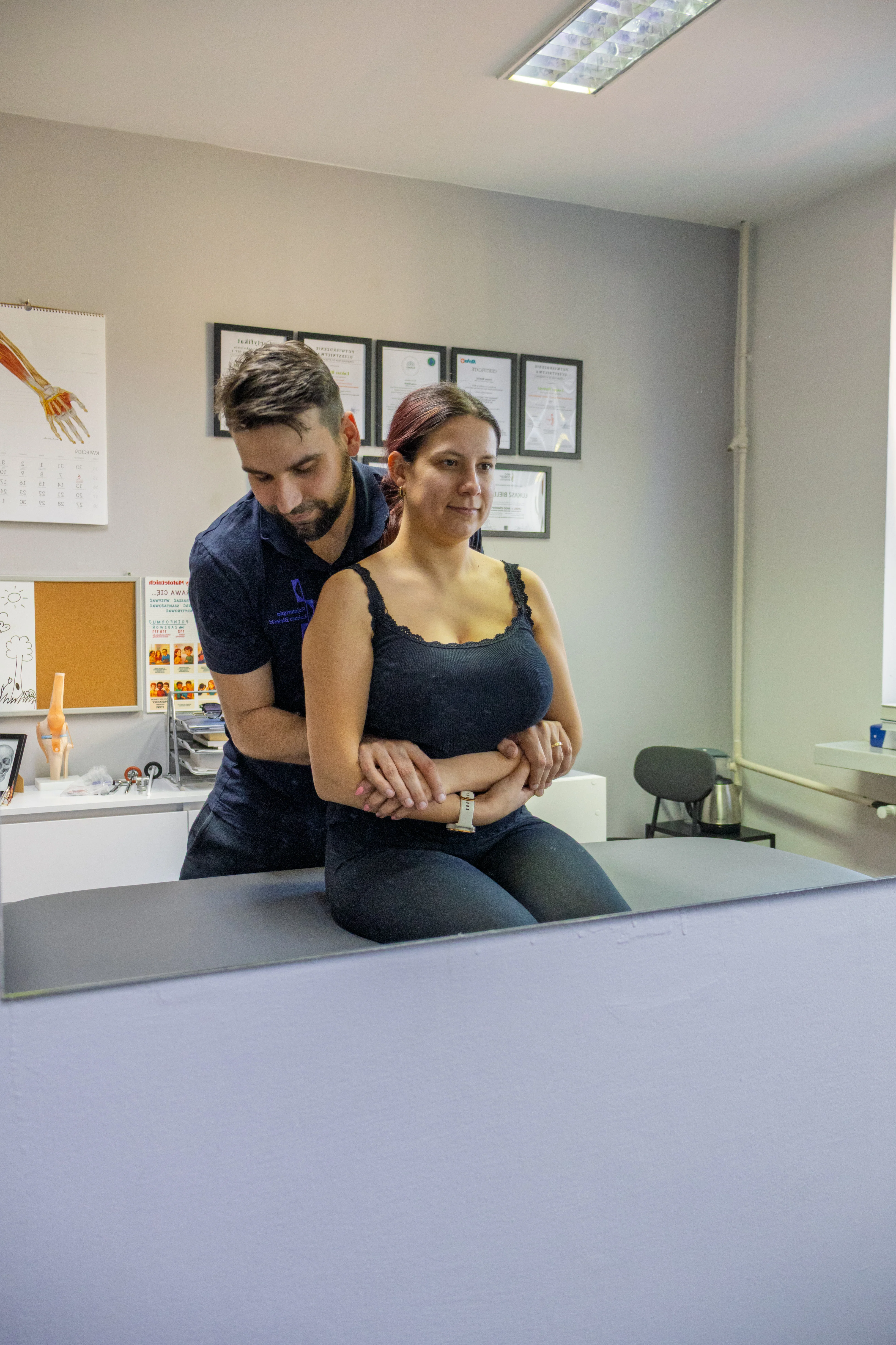 Fizjoterapeuta wykonujący mobilizację kręgosłupa u pacjentki siedzącej na stole